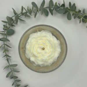 Kaars in doorzichtige glazen pot. Onderste laag is wit kaarsvet. Vervolgens doorzichtige gel met gouden schilfers in. Een witte pioenkaars als versiering bovenaan.