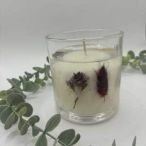 Witte kaars in doorzichtige glazen pot met zichtbare droogbloemen in verschillende kleuren.