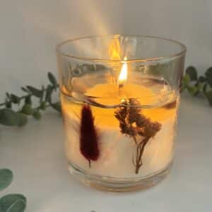 Witte kaars in doorzichtige glazen pot met zichtbare droogbloemen in verschillende kleuren.