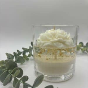 Kaars in doorzichtige glazen pot. Onderste laag is wit kaarsvet. Vervolgens doorzichtige gel met gouden schilfers in. Een witte pioenkaars als versiering bovenaan.