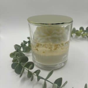 Kaars in doorzichtige glazen pot en goud deksel. Onderste laag is wit kaarsvet. Vervolgens doorzichtige gel met gouden schilfers in. Een witte pioenkaars als versiering bovenaan.