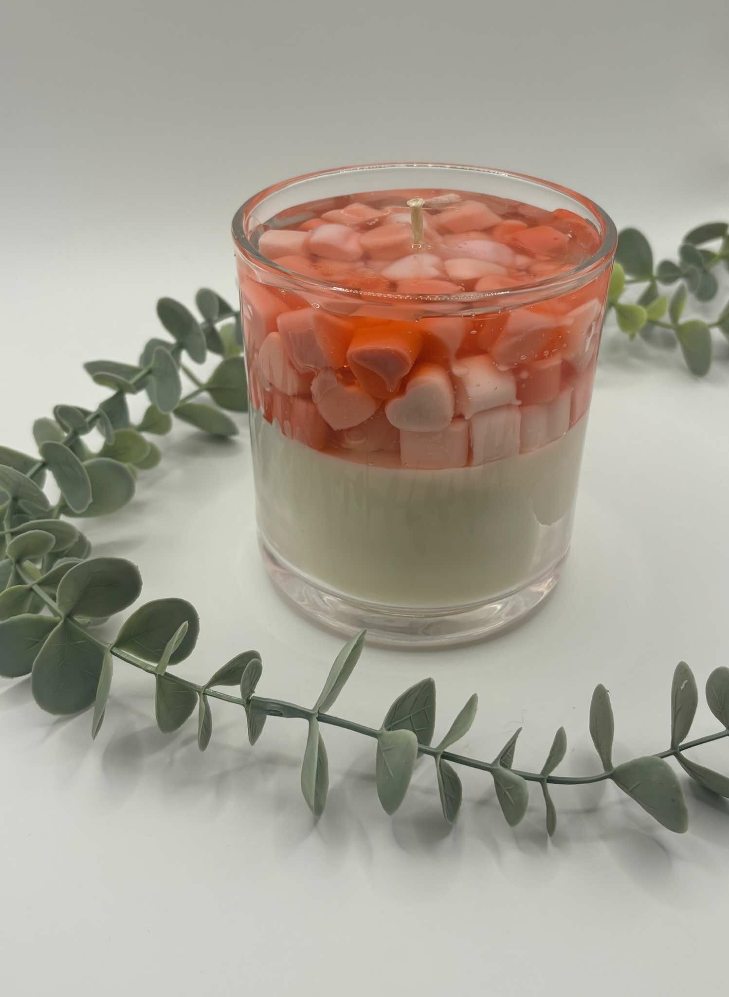 Kaars in doorzichtige glazen pot. Onderste laag is wit kaarsvet. Vervolgens doorzichtige gel met hartjes in verschillende rood tinten.