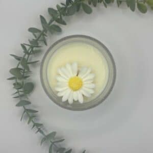 Kaars in doorzichtige glazen pot. Onderste laag is wit kaarsvet dat ruikt naar vanille. Er ligt een madeliefje bovenaan als versiering.