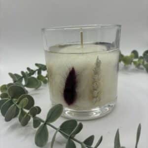 Witte kaars in doorzichtige glazen pot met zichtbare droogbloemen in verschillende kleuren.