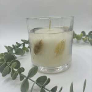 Witte kaars in doorzichtige glazen pot met zichtbare droogbloemen in verschillende kleuren.