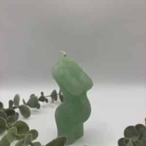 Een licht groene kaars in de vorm van een buste van een zwangere vrouw.