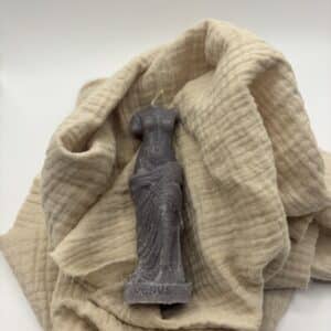 Een donker grijzen kaars in de vorm van een beeld van Venus zonder hoofd.