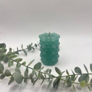 Een groene kaars in de vorm van een cilinder met bolletjes.