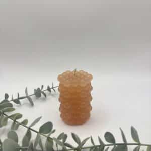 Een oranje kaars in de vorm van een cilinder met bolletjes.