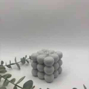 Een grijze kaars in de vorm van een medium kubus met bolletjes.