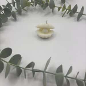 Een witte kaars in de vorm van een schelp met een parel in.