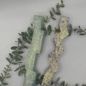 Een set van 2 kaarsen in de vorm van een pilaar. Een licht groene kaars in de vorm van een pilaar bestaande uit 4 blokken op elkaar en een een roze kaars in de vorm van een pilaar met zigzag-patroon. Beiden met holografische glitters.